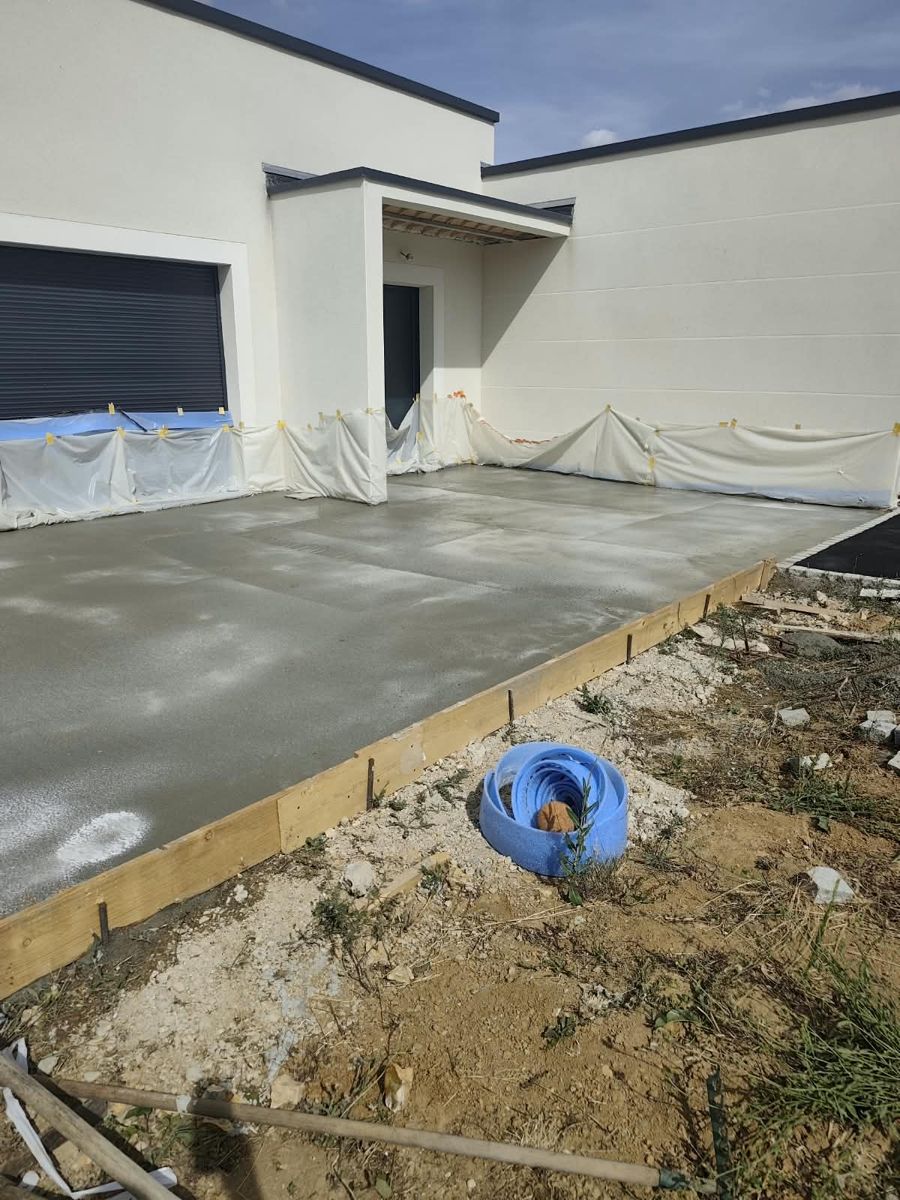 Grande dalle en béton coulée devant une maison neuve, coffrage bois en bordure